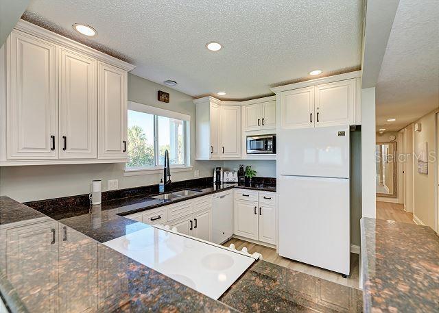 kitchen featuring sink, light hardwood / wood-style flooring, dark stone counters, white appliances, and white cabinets