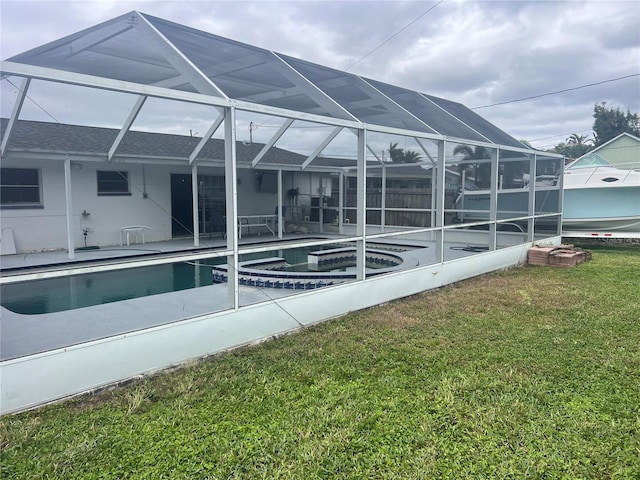 rear view of house featuring glass enclosure, a pool with hot tub, and a yard