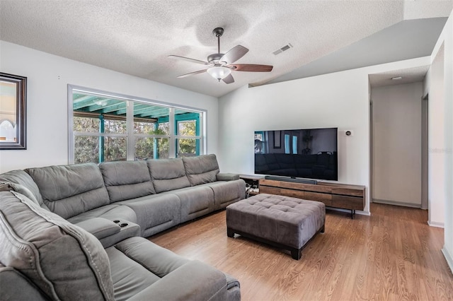 living room with visible vents, ceiling fan, lofted ceiling, light wood-style flooring, and a textured ceiling