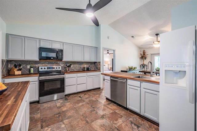 kitchen with ceiling fan, butcher block counters, vaulted ceiling, stainless steel appliances, and a sink