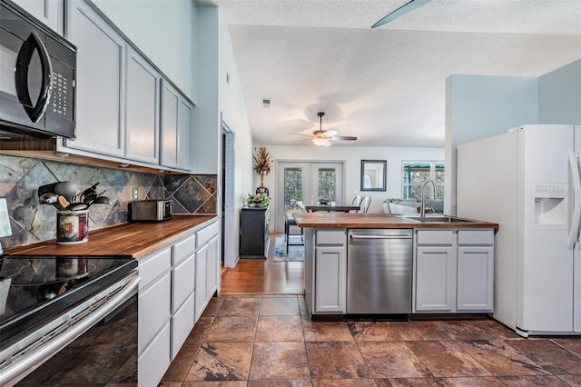 kitchen featuring wooden counters, a peninsula, a sink, decorative backsplash, and appliances with stainless steel finishes