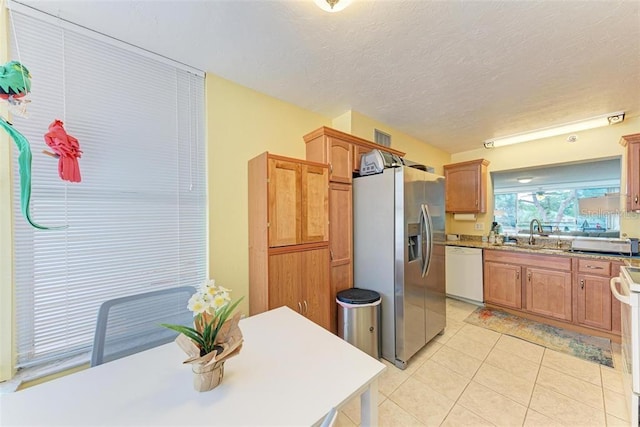 kitchen with a textured ceiling, sink, light tile patterned floors, and white appliances