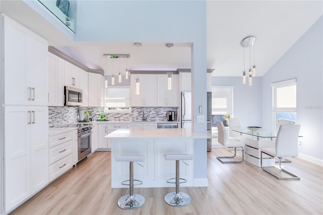 kitchen featuring pendant lighting, stainless steel appliances, white cabinetry, and light hardwood / wood-style floors