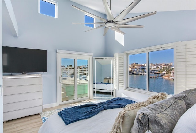 bedroom with ceiling fan, a high ceiling, access to outside, a water view, and light wood-type flooring