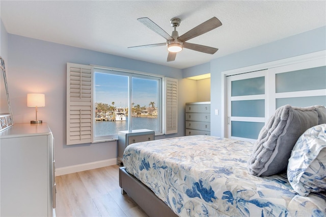 bedroom with ceiling fan, a water view, a textured ceiling, and light hardwood / wood-style flooring