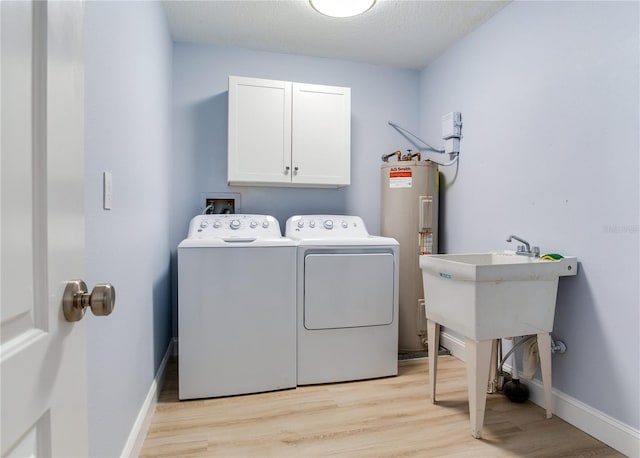 clothes washing area with light wood-type flooring, electric water heater, washing machine and dryer, and cabinets