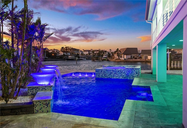 pool at dusk with an in ground hot tub, pool water feature, a water view, and a patio area