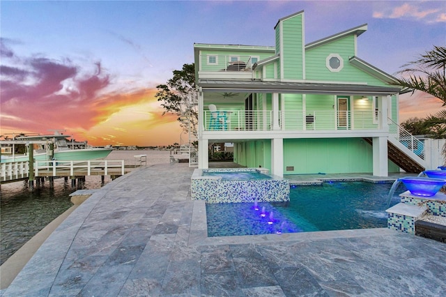 exterior space with a patio, a balcony, an in ground hot tub, pool water feature, and a water view