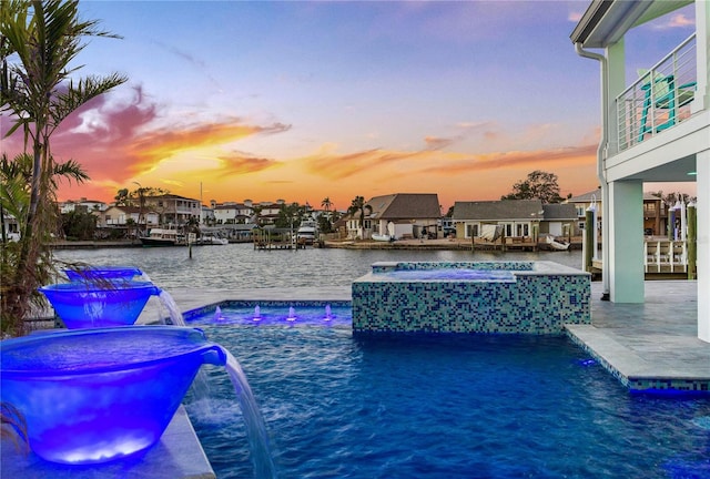 pool at dusk featuring an in ground hot tub, pool water feature, a water view, and a patio