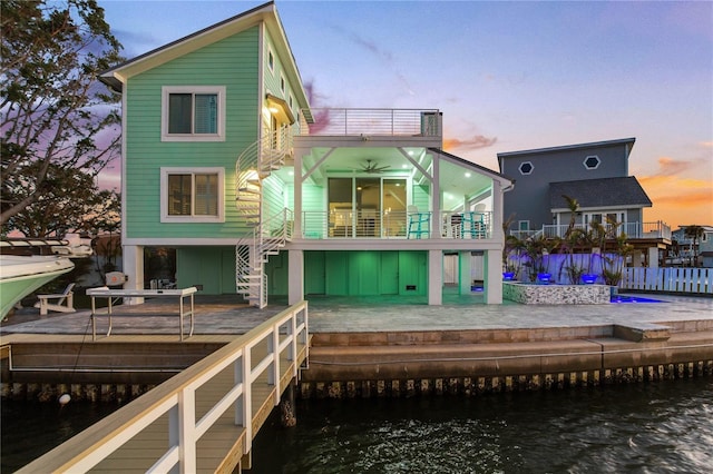 back house at dusk featuring ceiling fan, a balcony, a deck with water view, and a patio