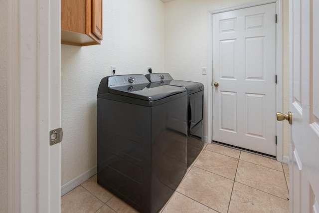 clothes washing area featuring baseboards, washing machine and dryer, cabinet space, and light tile patterned floors