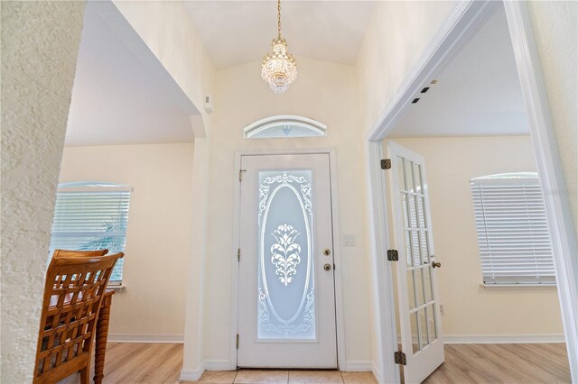 foyer featuring light wood-style flooring, baseboards, a notable chandelier, and arched walkways