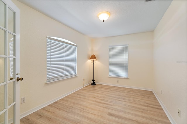 empty room with baseboards, french doors, and light wood finished floors