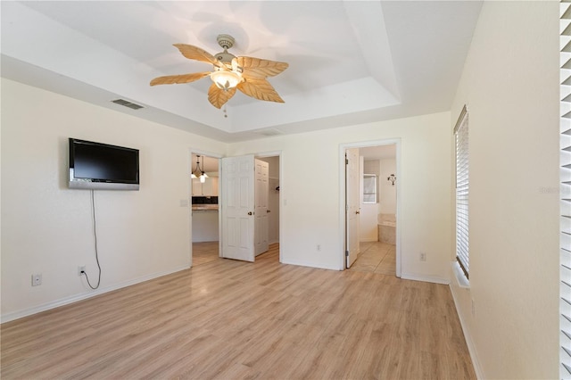 unfurnished bedroom with a tray ceiling, a spacious closet, baseboards, light wood finished floors, and visible vents