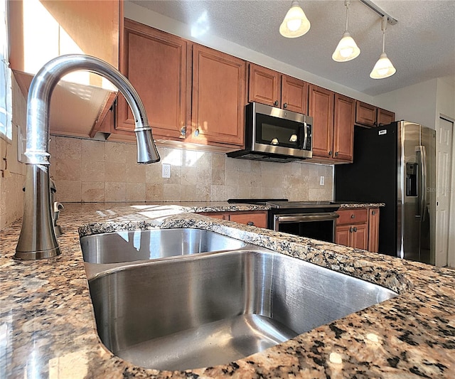 kitchen with light stone countertops, hanging light fixtures, appliances with stainless steel finishes, and tasteful backsplash