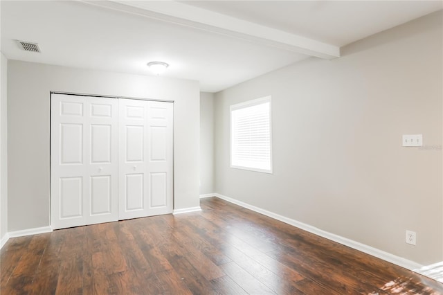 unfurnished bedroom featuring beamed ceiling, dark hardwood / wood-style floors, and a closet