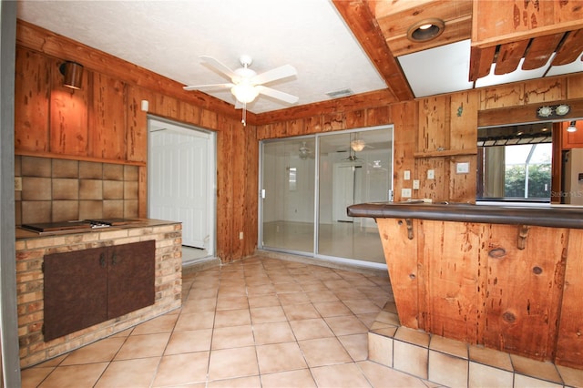 kitchen with light tile patterned floors, ceiling fan, and wood walls