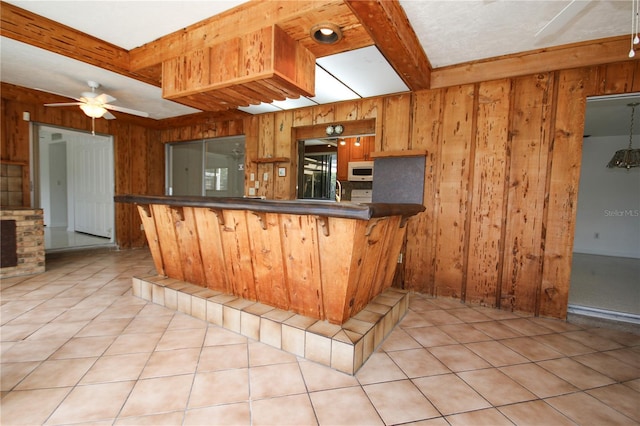 kitchen featuring light tile patterned flooring, wood walls, beam ceiling, and kitchen peninsula