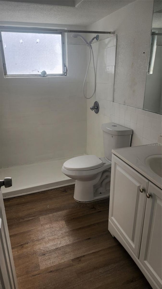 bathroom with a tile shower, vanity, tile walls, hardwood / wood-style floors, and toilet