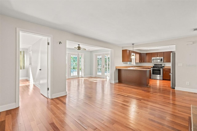 kitchen with french doors, light hardwood / wood-style flooring, decorative light fixtures, kitchen peninsula, and stainless steel appliances