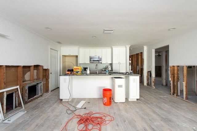 kitchen featuring dark stone counters, white cabinets, sink, an island with sink, and light hardwood / wood-style floors