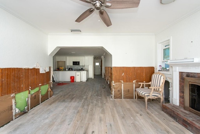 unfurnished room with ceiling fan, light hardwood / wood-style flooring, ornamental molding, and a brick fireplace