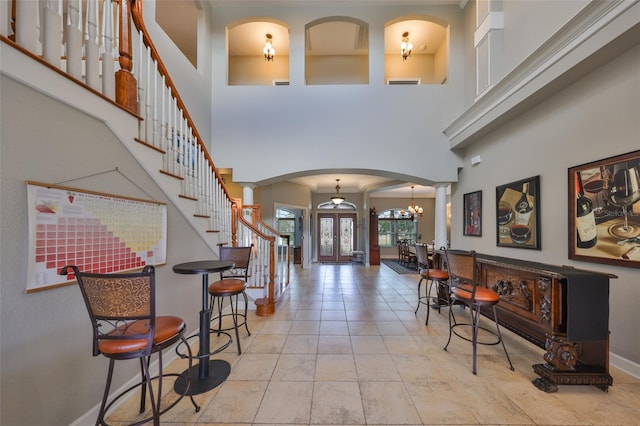 foyer with french doors, a chandelier, a high ceiling, and ornate columns