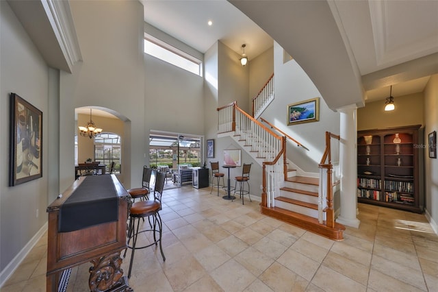 staircase with tile patterned flooring, a high ceiling, an inviting chandelier, and ornate columns