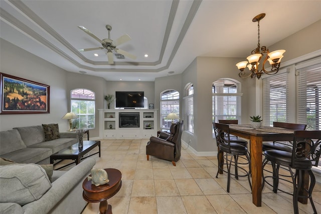 living room featuring a tray ceiling, ceiling fan with notable chandelier, ornamental molding, and light tile patterned flooring