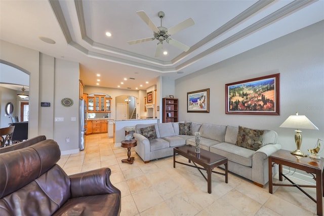 living room with a raised ceiling, crown molding, and ceiling fan