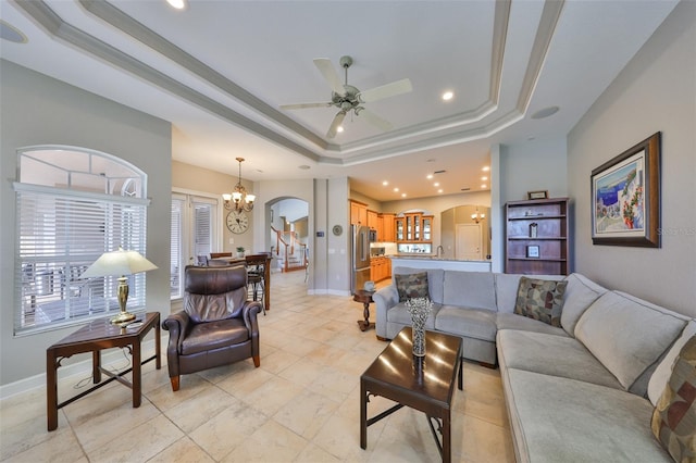 living room with ceiling fan with notable chandelier, ornamental molding, and a raised ceiling