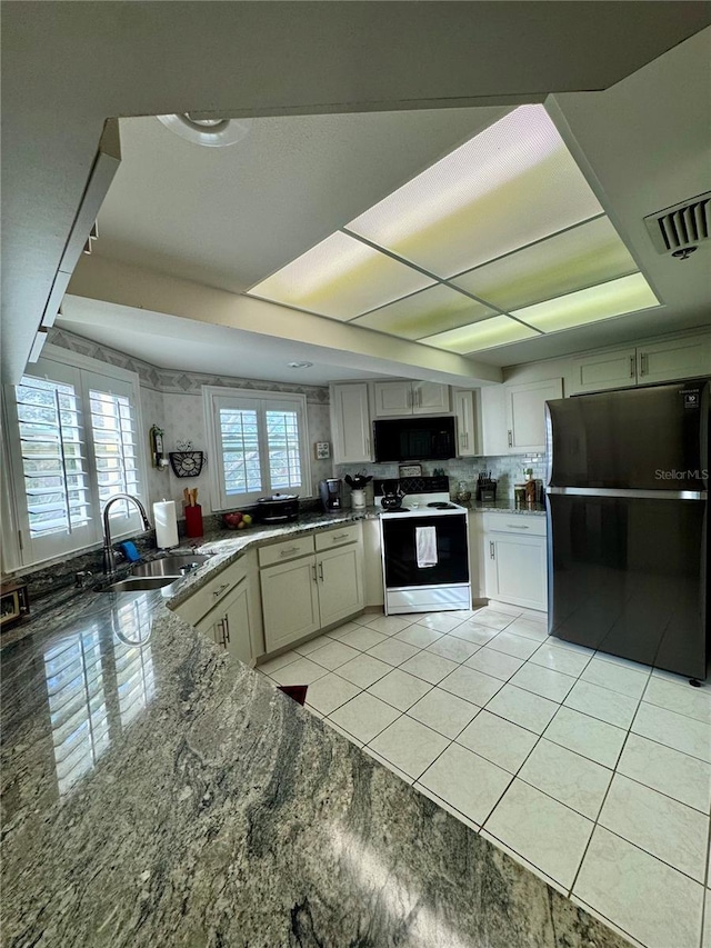 kitchen featuring sink, stone countertops, light tile patterned floors, decorative backsplash, and black appliances