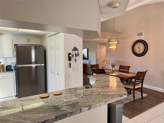 kitchen featuring decorative light fixtures, lofted ceiling, white cabinets, stainless steel fridge, and light stone counters