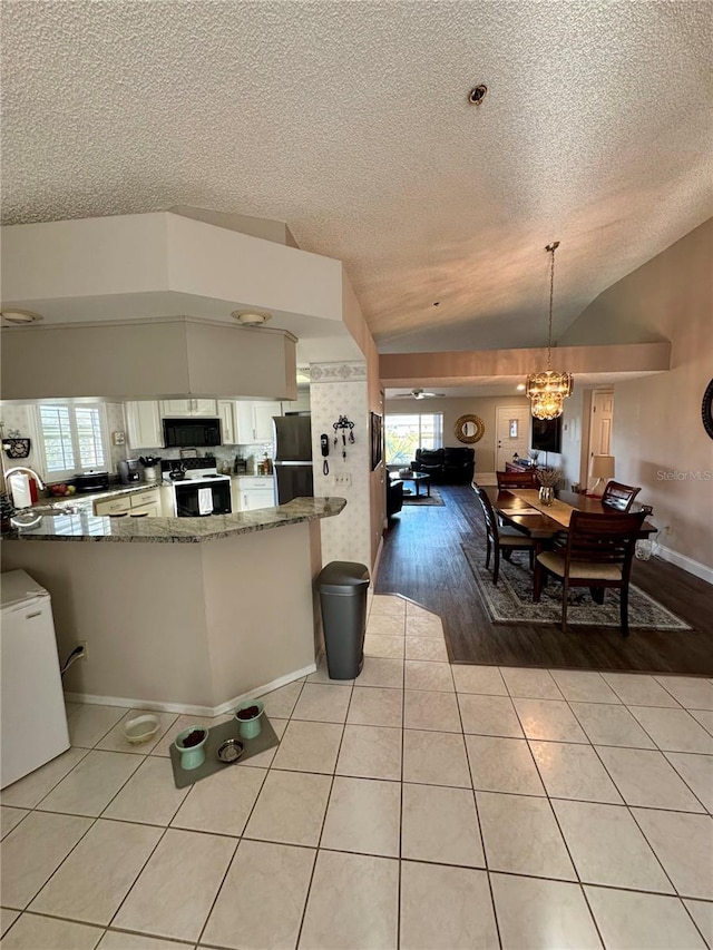 kitchen featuring pendant lighting, refrigerator, range with electric cooktop, kitchen peninsula, and dark stone counters