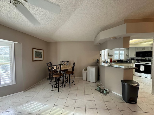 kitchen with light tile patterned floors, white range with electric stovetop, light stone counters, vaulted ceiling, and kitchen peninsula