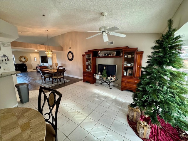 tiled living room featuring ceiling fan with notable chandelier, vaulted ceiling, and a textured ceiling