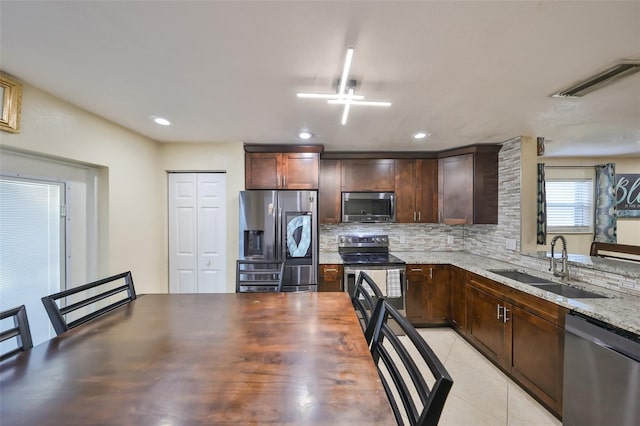 kitchen with light stone countertops, appliances with stainless steel finishes, backsplash, sink, and light tile patterned floors