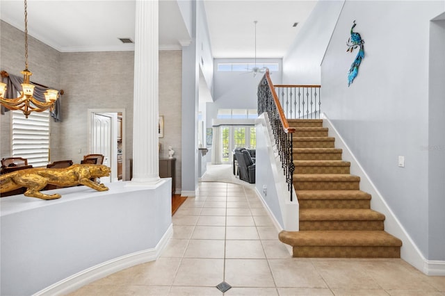 foyer entrance featuring ornate columns, a high ceiling, crown molding, light tile patterned floors, and ceiling fan with notable chandelier