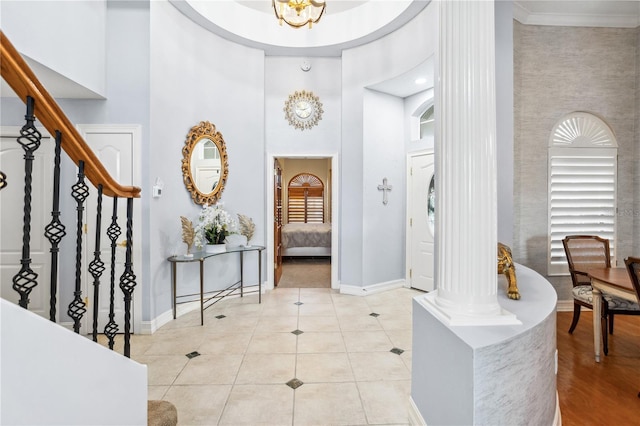 tiled entryway with decorative columns, crown molding, a towering ceiling, and a notable chandelier