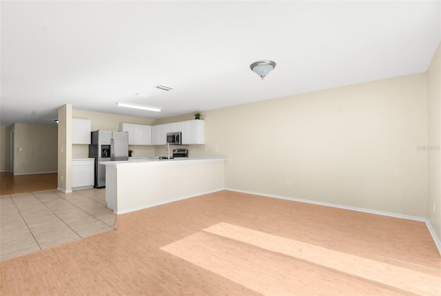 kitchen featuring kitchen peninsula, appliances with stainless steel finishes, light tile patterned floors, and white cabinetry