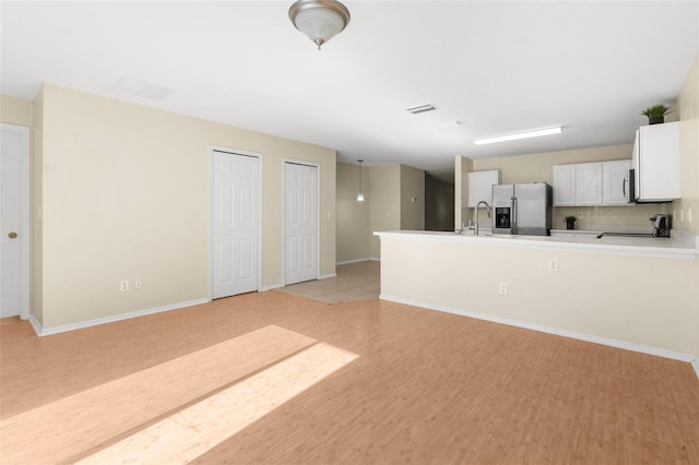 kitchen featuring stove, stainless steel fridge, light wood-type flooring, tasteful backsplash, and white cabinetry