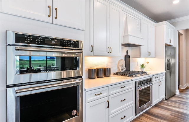 kitchen featuring appliances with stainless steel finishes, premium range hood, ornamental molding, light hardwood / wood-style flooring, and white cabinetry