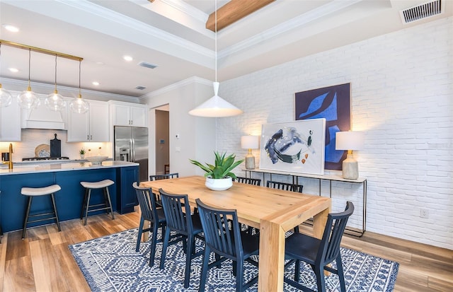 dining room featuring brick wall, light wood-type flooring, and ornamental molding