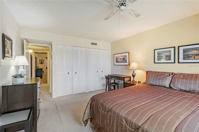 bedroom featuring a textured ceiling, ceiling fan, light carpet, and multiple closets