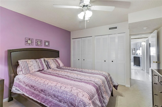 bedroom with two closets, ceiling fan, light colored carpet, and a textured ceiling