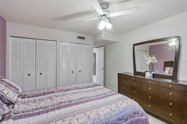 carpeted bedroom with ceiling fan, a textured ceiling, and two closets