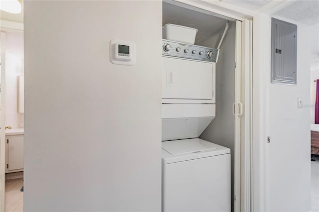 washroom featuring a textured ceiling, electric panel, tile patterned flooring, and stacked washer / drying machine