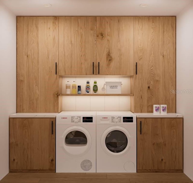 clothes washing area featuring washer and clothes dryer, cabinets, and light wood-type flooring