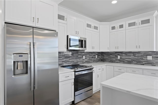 kitchen with appliances with stainless steel finishes, tasteful backsplash, light stone counters, hardwood / wood-style flooring, and white cabinetry