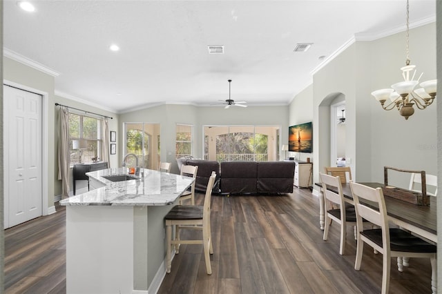 kitchen featuring sink, dark wood-type flooring, a kitchen island with sink, hanging light fixtures, and light stone counters